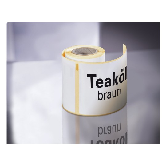 De afbeelding toont een rol met een label voor teakolie, gekleurd bruin. De rol heeft een glanzende afwerking en reflecteert op een oppervlak.