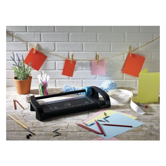 De afbeelding toont een creatieve werkplek met een snijmachine, gekleurde papieren, potloden, washi-tape en een plant. Aan een touw hangen verschillende gekleurde kaarten.