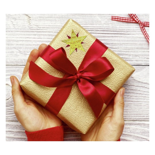 Dit is een gouden cadeau verpakt met een rode strik. Het heeft een stervormige sticker met wensen. De handen van een persoon houden het cadeau vast.