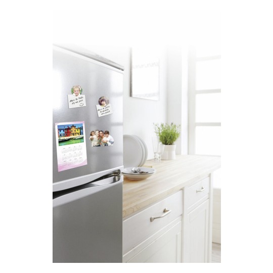 Op de afbeelding staat een koelkast met foto's en notities erop. Achter de koelkast is een houten tafel met een paar borden en een plantenpot. De omgeving is helder en heeft een moderne uitstraling.