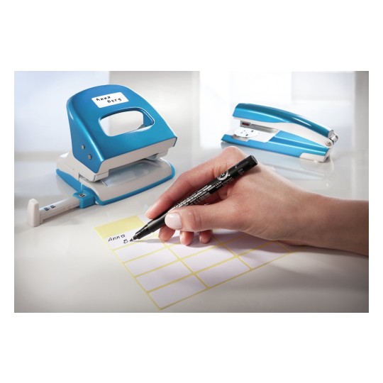 In de afbeelding is een blauwe perforator en een blauwe nietmachine te zien. Iemand schrijft met een zwarte stift op een gele label, met een naam erop.