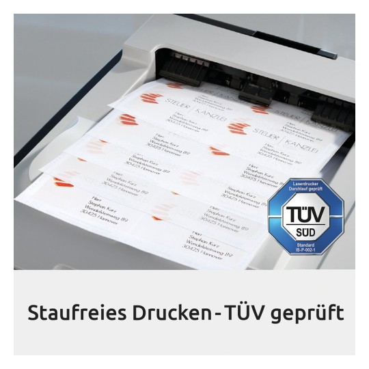 De afbeelding toont een laserprinter die visitekaartjes afdrukt. Er zijn meerdere kaarten zichtbaar met namen en adressen. Daarnaast is er een TÜV-keurmerk zichtbaar, wat aangeeft dat het apparaat getest is.