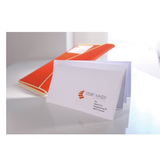 De afbeelding toont een witte envelop met een visitekaartje voor een belastingadvieskantoor op een bureau, met een oranje map op de achtergrond.