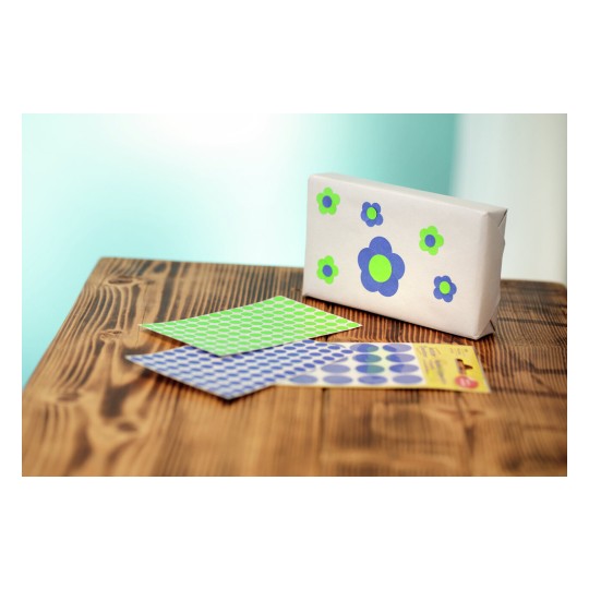 Afbeelding van een ingepakt cadeau met bloemstickers, en twee vellen met kleurige stippenstickers op een houten tafel.