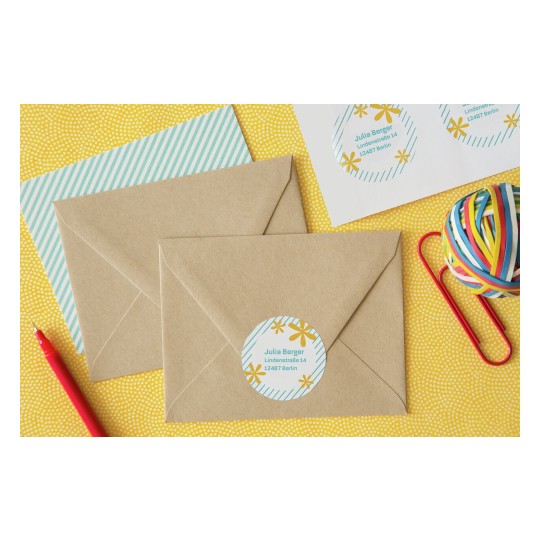 De afbeelding toont meerdere bruine enveloppen met een adressticker, een vel met gestreept papier, een potlood, en een bundel elastiekjes op een gele achtergrond.