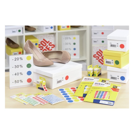 De afbeelding toont een paar beige schoenen bovenop een witte doos. Er zijn verschillende dozen en etiketten in de achtergrond, met kortingen aangegeven in percentages. Kleuretiketten in groen, geel, blauw en rood liggen op tafel.