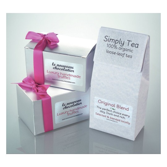 Het beeld toont luxe handgemaakte truffels in zilveren dozen met een roze strik en een pakje losse thee met de tekst 'Simply Tea' en 'Original Blend'.