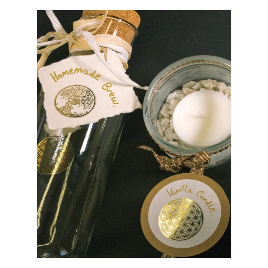 De afbeelding toont een glazen fles met een kurk, gemerkt met 'Homemade Brew' en een kaars in een glazen houder met witte stenen. De kaars heeft een label met 'Vanilla Candle'.