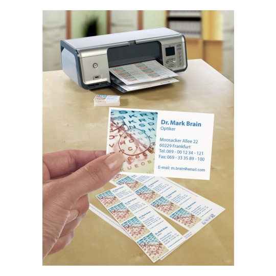In de afbeelding is een printer te zien die visitekaartjes afdrukt. De kaartjes bevatten de naam en contactinformatie van een opticien genaamd Dr. Mark Brain. Een hand houdt een van de kaartjes vast, terwijl andere kaartjes naast de printer liggen.