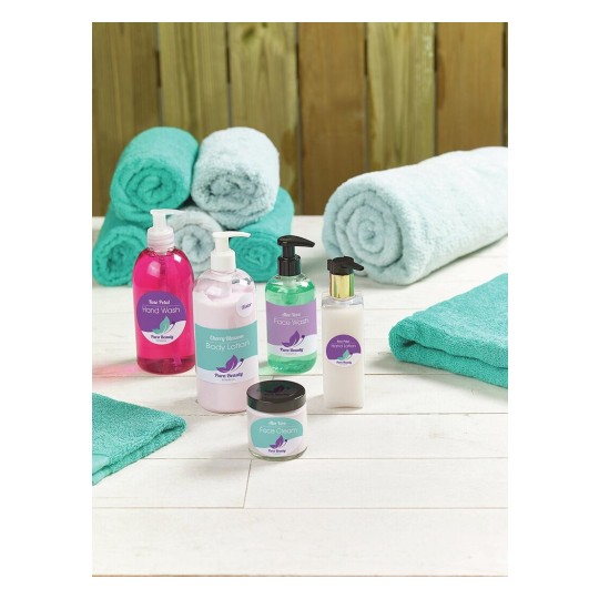 De afbeelding toont een collectie van verzorgingsproducten, waaronder handwas, lichaamslotion, gezichtswash en gezichtscrème, met enkele opgerolde handdoeken. De producten zijn kleurrijk en hebben etiketten met de naam 'Pura Beauty'.