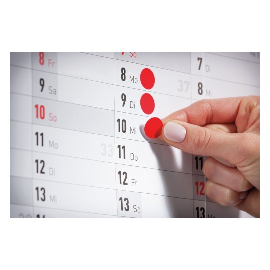 Een hand plakt een rode stip op een kalender, met de focus op de datum 10, die een woensdag is.
