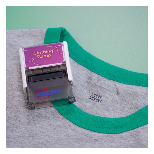 Dit beeld toont een kledingstempel met de tekst 'Clothing Stamp' bovenop een grijs shirt met groene hals.