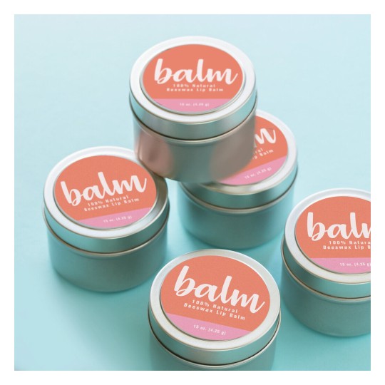 De afbeelding toont een aantal metalen blikjes lippenbalsem, die gestapeld zijn. Elk blikje heeft een etiket met de tekst 'balm' en de vermelding '100% Natural Beeswax Lip Balm'. De blikjes zijn op een lichtblauwe achtergrond geplaatst.