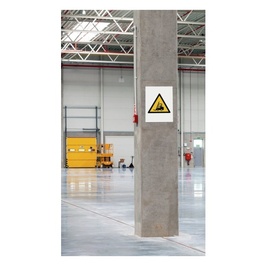 Het beeld toont een grote, lege opslagruimte met een betonnen pilaar. Aan de pilaar hangt een waarschuwingsbord met een afbeelding van een heftruck. Achteraan is een gele deur en er zijn enkele machines zichtbaar.