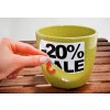 Afbeelding van een groene pot met een kortingslabel van 20% erop. Een hand verwijdert een sticker van de pot op een houten ondergrond.