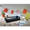 De afbeelding toont een creatieve werkplek met een snijmachine, gekleurde papieren, potloden, washi-tape en een plant. Aan een touw hangen verschillende gekleurde kaarten.