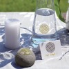 Op de afbeelding staat een tafel met een witte kaars, een karaf water, en een grijze steen met een boomontwerp. Daarnaast ligt een kaartje met de tekst 'Veel Kracht!' en een cirkelontwerp. De tafelkleed is lichtgrijs met patronen.