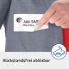 In de afbeelding ziet u een hand die een label uit een zak van een grijze jas trekt. Het label heeft de naam 'Julia SMITH Marketing' en de tekst 'Rückstandsfrei ablösbar', wat betekent dat het vrij kan worden verwijderd zonder resten achter te laten.