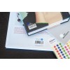 De afbeelding toont een stapel boeken met zichtbare barcodes en een vel met kleurrijke stippen. Op de achtergrond staat een Franse tekst over Sébastien Bouillet.