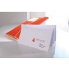 De afbeelding toont een witte envelop met een visitekaartje voor een belastingadvieskantoor op een bureau, met een oranje map op de achtergrond.