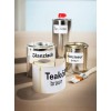 De afbeelding toont verschillende blikken verf en een kwast. Er zijn metalen blikken met labels zoals 'Glanzlack', 'Holzlazur', en een pot met 'Terpentin' in het midden. Daarnaast ligt er een rol met 'Teaköl' op een houten oppervlak.