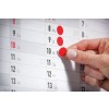 Een hand plakt een rode stip op een kalender, met de focus op de datum 10, die een woensdag is.