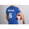 Een man in een blauw voetbalshirt met de naam 'HUGO' en het nummer 6, houdt een voetbal vast.