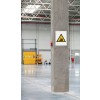 Het beeld toont een grote, lege opslagruimte met een betonnen pilaar. Aan de pilaar hangt een waarschuwingsbord met een afbeelding van een heftruck. Achteraan is een gele deur en er zijn enkele machines zichtbaar.